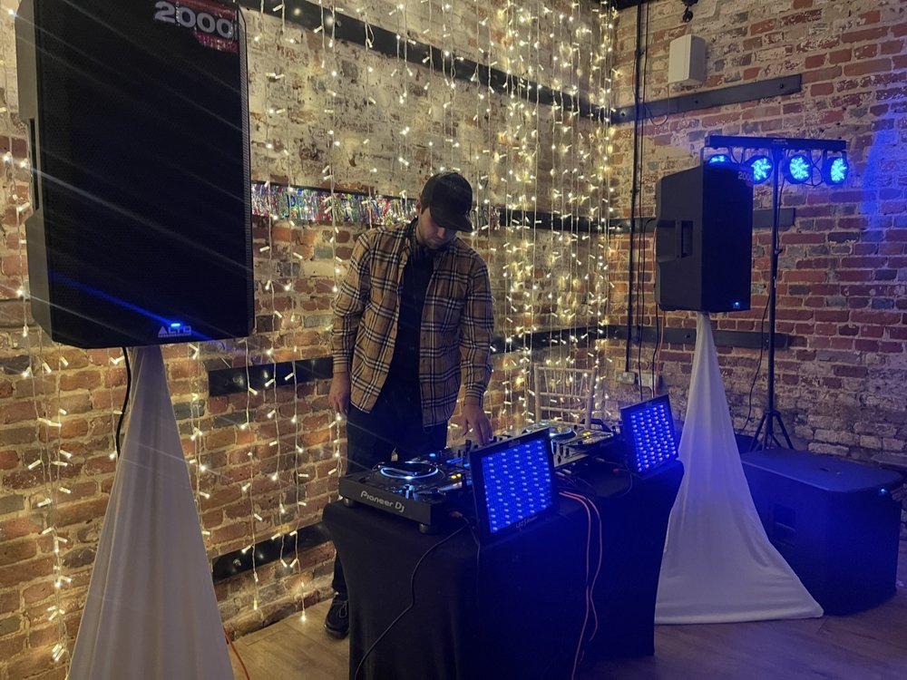 DJ setup with speakers and a wall of fairy lights in a brick venue