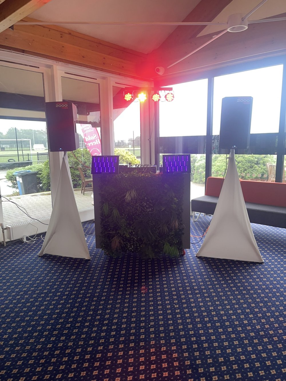 Speakers, lighting and a DJ booth with a green foliage front
